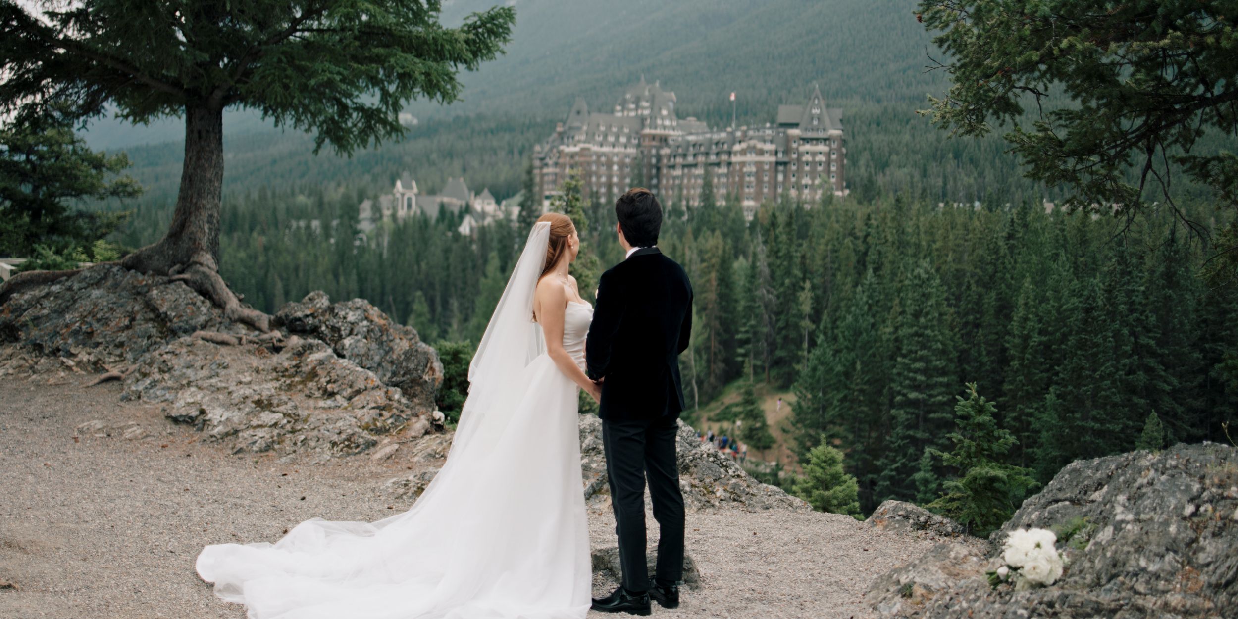 Bride and groom overlooking Bow Falls with the Fairmont Banff Springs Hotel in the background during a wedding in Banff National Park.